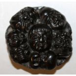 A JAPANESE WOOD NOH MULTIPLE MASK NETSUKE, the flattened circular form modelled in relief with