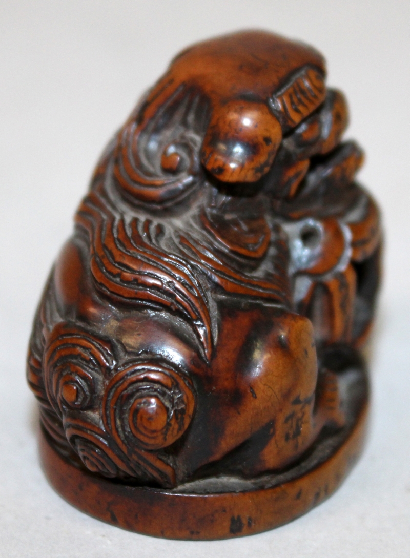 A JAPANESE CARVED WOOD NETSUKE OF A BUDDHISTIC LION, it's head resting on a pierced ribboned ball, - Image 2 of 5