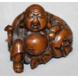 A JAPANESE MEIJI PERIOD CARVED WOOD NETSUKE OF HOTEI, the deity holding a fan and leaning back