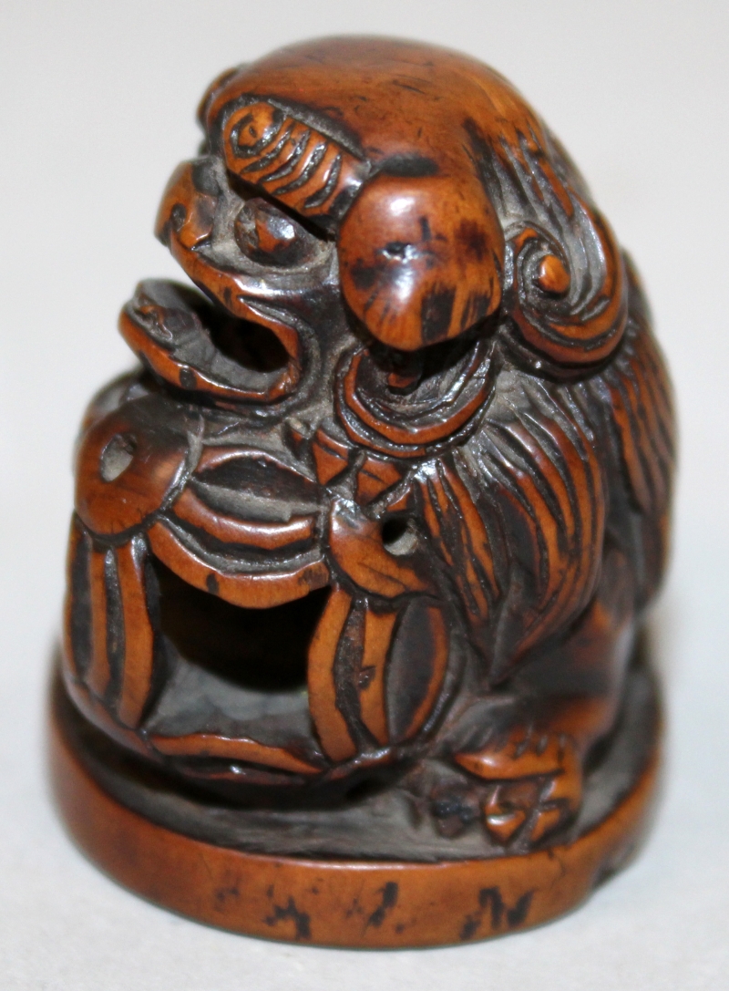 A JAPANESE CARVED WOOD NETSUKE OF A BUDDHISTIC LION, it's head resting on a pierced ribboned ball, - Image 4 of 5