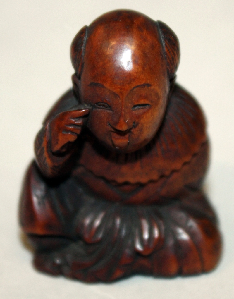 A JAPANESE MEIJI PERIOD WOOD NETSUKE OF A SEATED BOY, with protruding tongue, and holding an oni