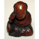 A JAPANESE MEIJI PERIOD WOOD NETSUKE OF A SEATED BOY, with protruding tongue, and holding an oni