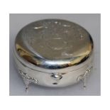 A silver circular ring box with engraved lid, on four curving legs.