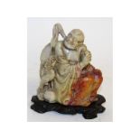 A Chinese carved soapstone seated figure with dragon, 4.75ins high, on a wooden stand.