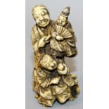 A JAPANESE MEIJI PERIOD STAINED IVORY OKIMONO OF A PUPPETEER, in the company of a boy and a dog, the