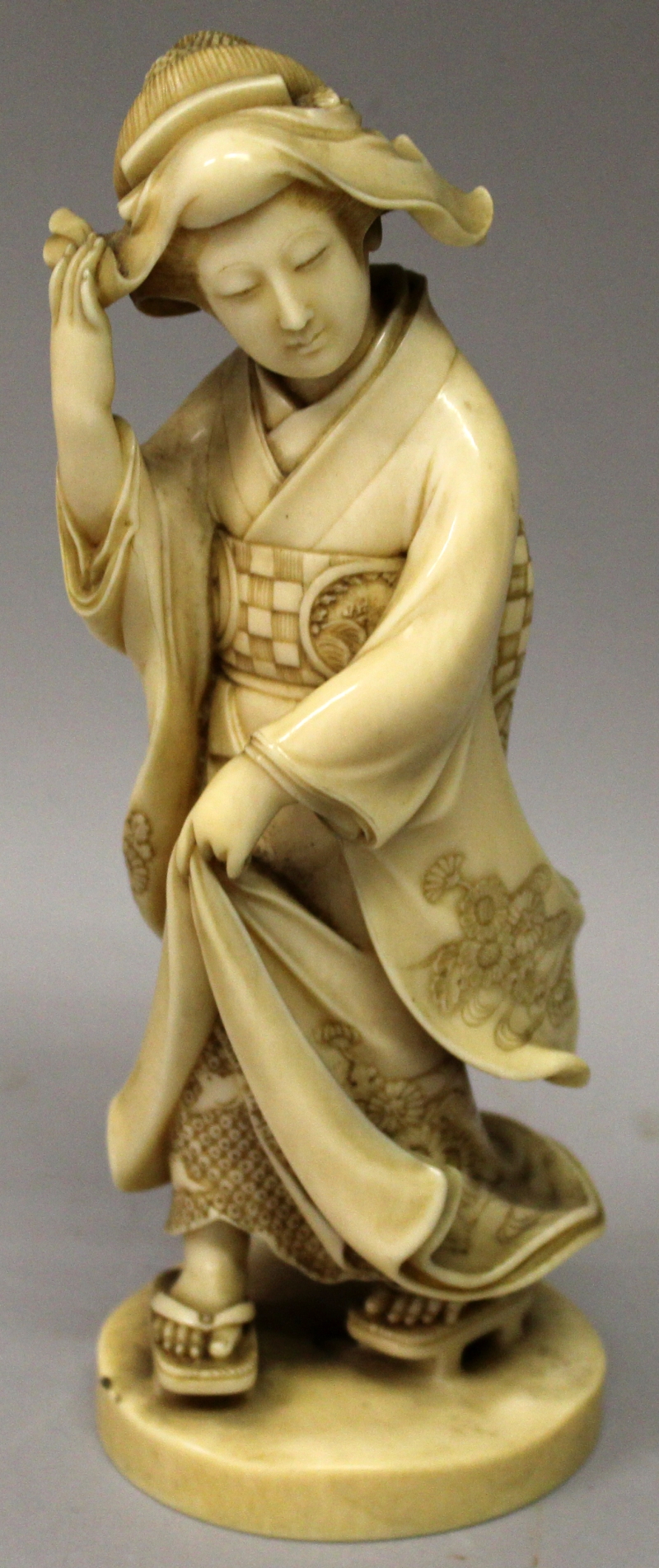 A GOOD QUALITY SIGNED JAPANESE MEIJI PERIOD IVORY OKIMONO OF A BIJIN, walking on geta in floral