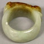 A CHINESE CELADON JADE RING, carved in relief with a resting chilong, the stone with russet