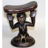 A CARVED WOOD TRIBAL HEAD REST. 9ins high.