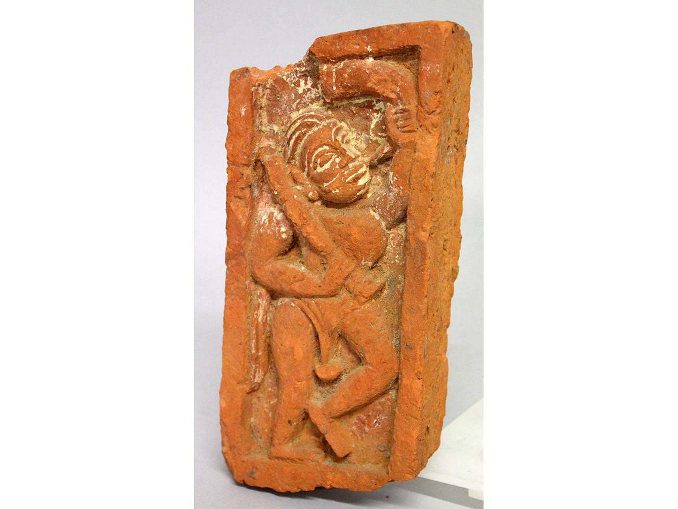 AN EARLY INDIAN CARVED RED BRICK, man blowing a horn. 8.5ins long, 4ins wide.