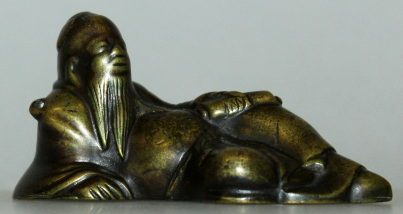 A 17TH CENTURY CHINESE BRONZE WATERDROPPER, cast in the form of a reclining sage, 3.75in wide & 1.