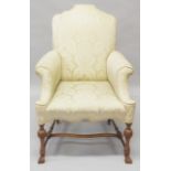 A GEORGE II DESIGN WALNUT AND UPHOLSTERED ARMCHAIR, with hump back, scrolling arms on turned and