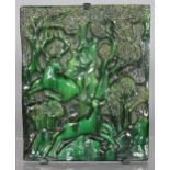 A LARGE ART DECO GREEN GLAZED TILE depicting deer in a wooded setting. 16ins high, 13ins wide.