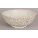 A CHINESE WHITE GLAZED PORCELAIN BOWL, the sides moulded with phoenix above waves, 8.25in diameter &