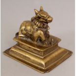 A 19TH CENTURY INDIAN BRONZE MODEL OF A NANDI BULL, recumbent and raised on a stepped plinth, 3.