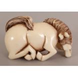 AN EARLY 20TH CENTURY SIGNED JAPANESE CARVED IVORY NETSUKE OF A KNEELING HORSE, its head turned to