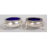 A SMALLER PAIR OF GEORGE V CIRCULAR SALTS, with sapphire blue liners, on three pad feet. London