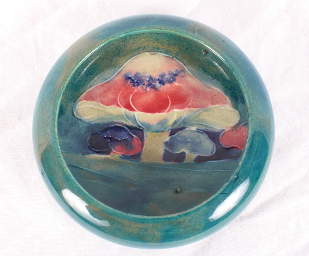 A Moorcroft "Claremont" pattern dish with inverted rim decorated toadstools on a green ground,