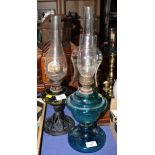 Two oil lamps with green and blue glass reservoirs, chimneys and shades