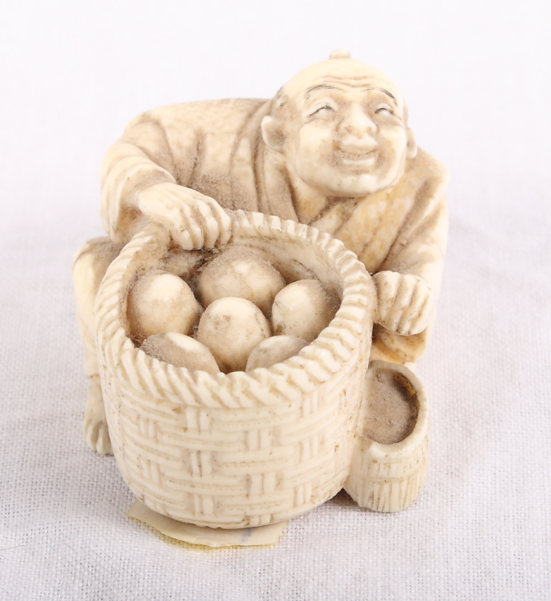 An ivory netsuke of a seated figure with a basket, signed