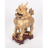 A Chinese gilt bronze censer formed as a Dog of Fo, on carved wooden base, 11" high