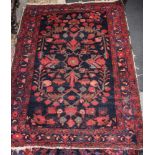 A Persian rug decorated stylised flowers in red and green on a dark blue ground with three border