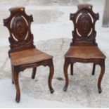 A pair of William IV carved oak hall chairs with panel seats and backs, on cabriole supports