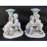 Two decorative porcelain candlesticks with embracing putti bases;