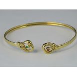 An 18ct gold bangle with abstract heart shaped terminals one set with ruby and diamonds the other