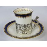 A Coalport bone china coffee can and saucer with repoussé silver sleeve (putti and dragon design)