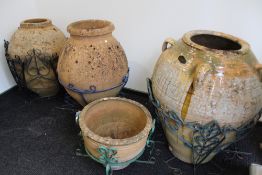 A GROUP OF LARGE TERRACOTTA OIL JARS IN WROUGHT IRON STANDS