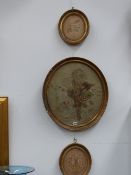 A Regency oval silkwork panel of a floral bouquet together with two others all in gilt frames