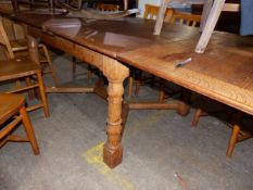 A LARGE OAK DRAW LEAF TABLE ON TURNED COLUMN SUPPORTS UNITED BY STRETCHER