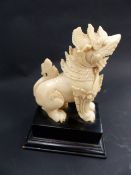 AN EASTERN CARVED IVORY FIGURE OF A MYTHICAL DRAGON/LION GUARDIAN MOUNTED ON HARDWOOD PLINTH. HEIGHT