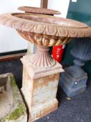 A SET OF FOUR CAST IRON BROAD RIM SHALLOW URNS ON FLUTED BASES SUPPORTED ON SQUARE PLINTHS.