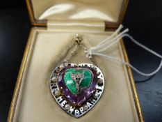 AN EARLY 20TH.C.MEMORIAL HEART SHAPED PENDANT WITH AMETHYST CENTRE, GREEN ENAMEL FLOWER MOTIF, THE