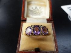 A 9CT. GOLD THREE STONE AMETHYST RING WITH DIAMOND POINTS