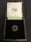 An Edwardian diamond and sapphire circular brooch / pendant with stylized foliate border. 2.2cm