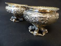 A pair of George IV silver gilded table salts with repousse cross dolphin supports. The border