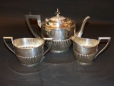 A silver three piece tea set with ribbed repousse decoration with ebonized handle and finial to