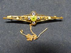 AN EDWARDIAN OPENWORK BAR BROOCH SET PERIDOT, SEED PEARLS. STAMPED 15CT