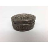 A small oval white metal Pill Box, the pull-off lid and body decorated with scrolled foliate detail,