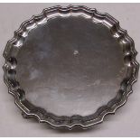 George V silver waiter of typical shaped form with polished field and raised on three cast and