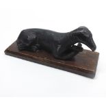 19th century cast metal model of a recumbent dog, raised on a wooden plinth base, approx 8" wide