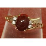 Modern 9ct gold dress ring, with central oval cabochon red stone, the pierced scroll shoulders set