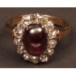 Precious metal garnet and diamond cluster ring, the centre oval cabochon cut garnet surrounded by 14