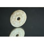 Chinese greyish-white jade ‘Bi’ disc, carved to one side with archaistic patterns, and the reverse