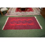 A Middle-Eastern floor rug with dark geometric designs against a red ground. Approximately 6' x 3.