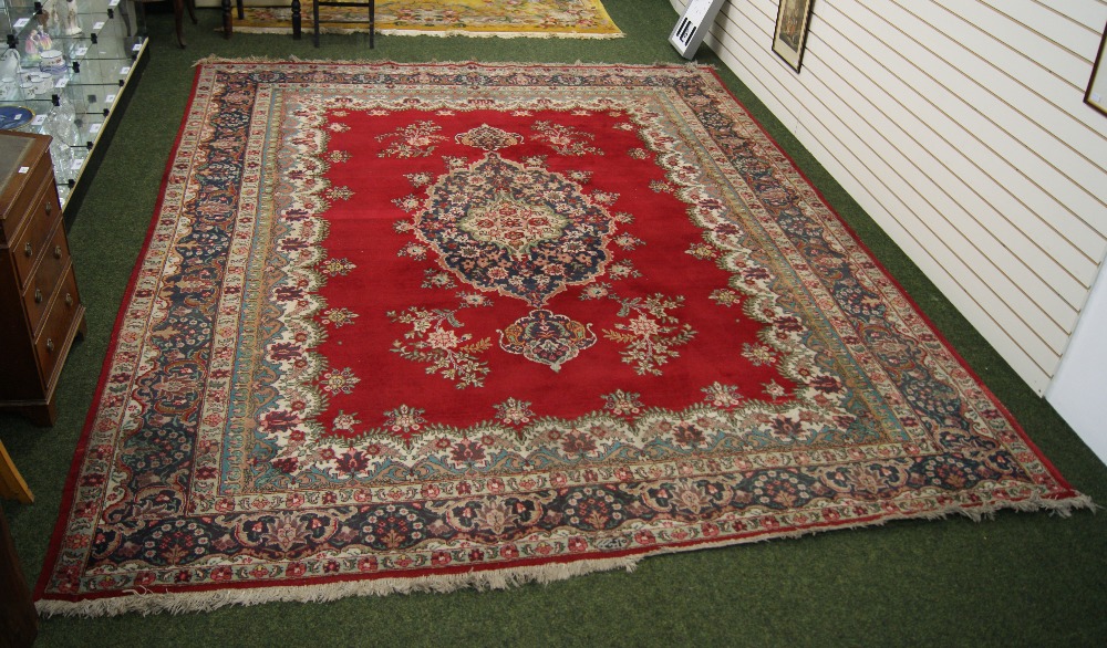 A traditional floor rug with floral decoration and geometric designs against a red and cream ground.