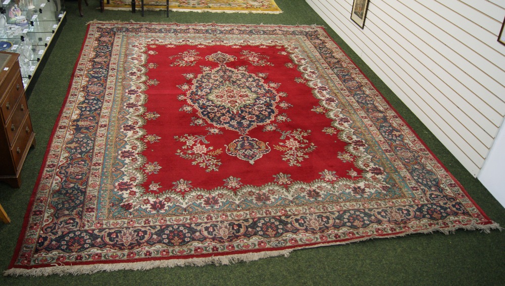 A traditional floor rug with floral decoration and geometric designs against a red and cream ground. - Image 2 of 2