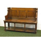 A 19th Century oak settle with a panelled back rest, turned supports and under-shelf.